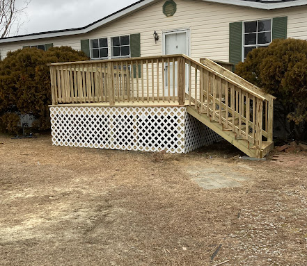 Light wood front entry deck with lattice skirting and staircase leading to a home