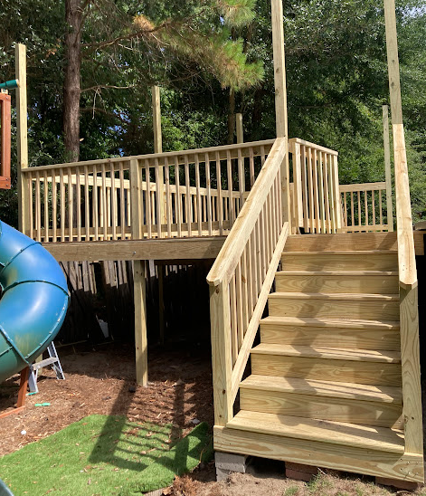 Custom wooden play structure deck with stairs and slide in a backyard